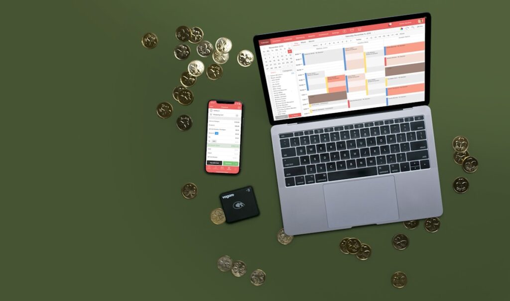 Laptop, phone, and coins on a desk for tracking income and expenses