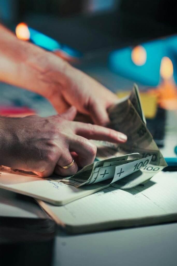 Hands counting money over a notebook for zero-based budget planning